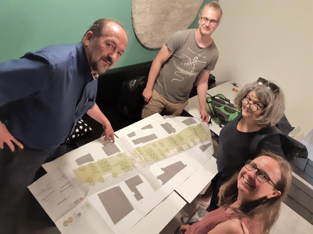 Vier Personen stehen bzw. siten um einen Tisch auf dem ein Plan von einem Park liegt.