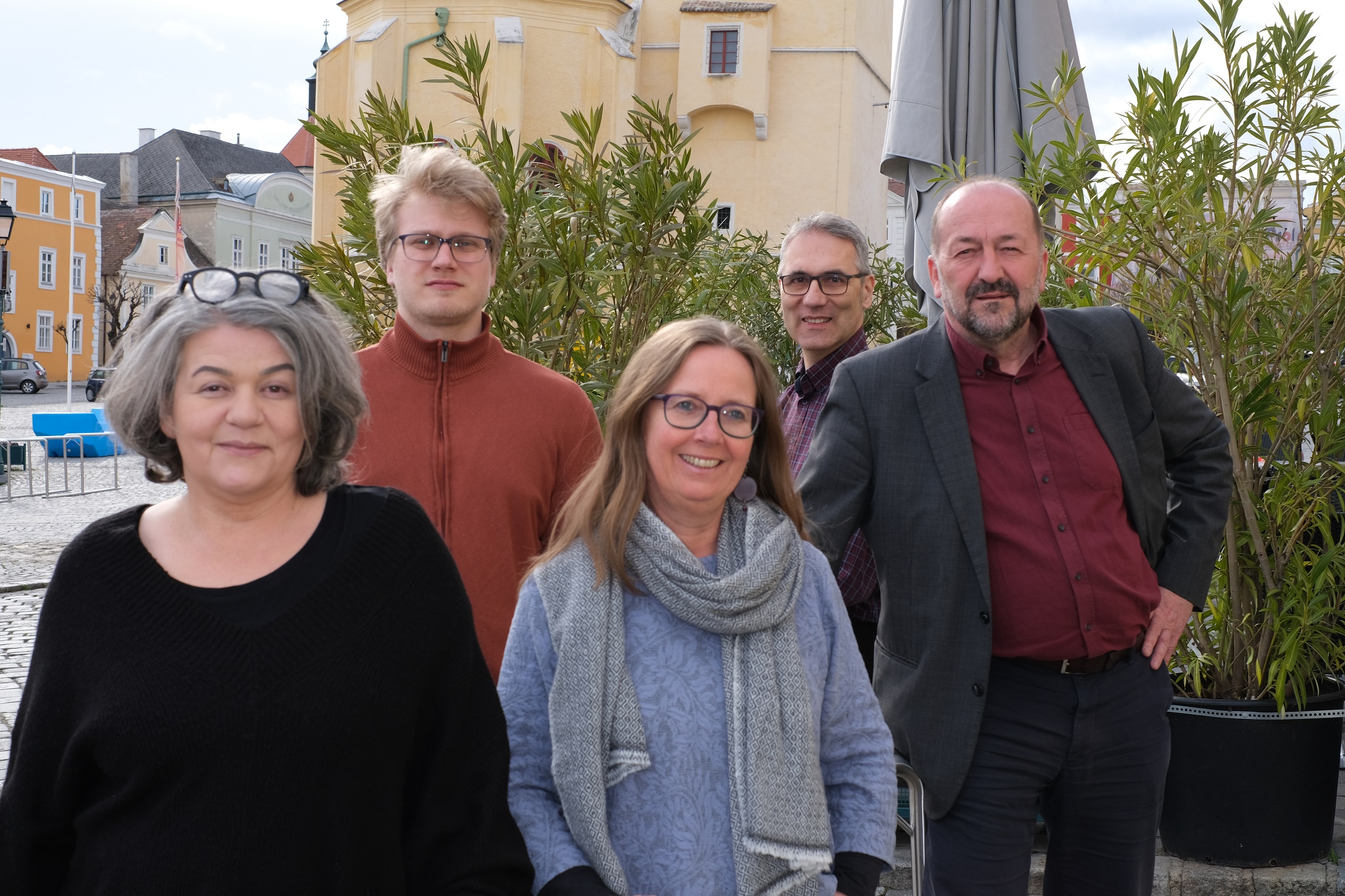 Gruppe von fünf Personen im Freien, die nebeneinender stehen und lächeln