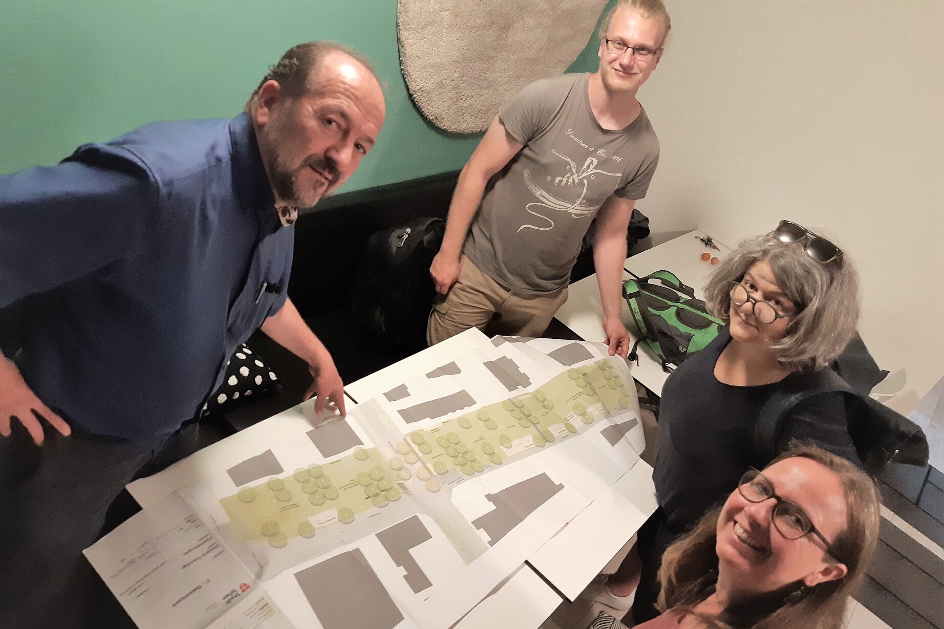 Vier Personen stehen bzw. siten um einen Tisch auf dem ein Plan von einem Park liegt.