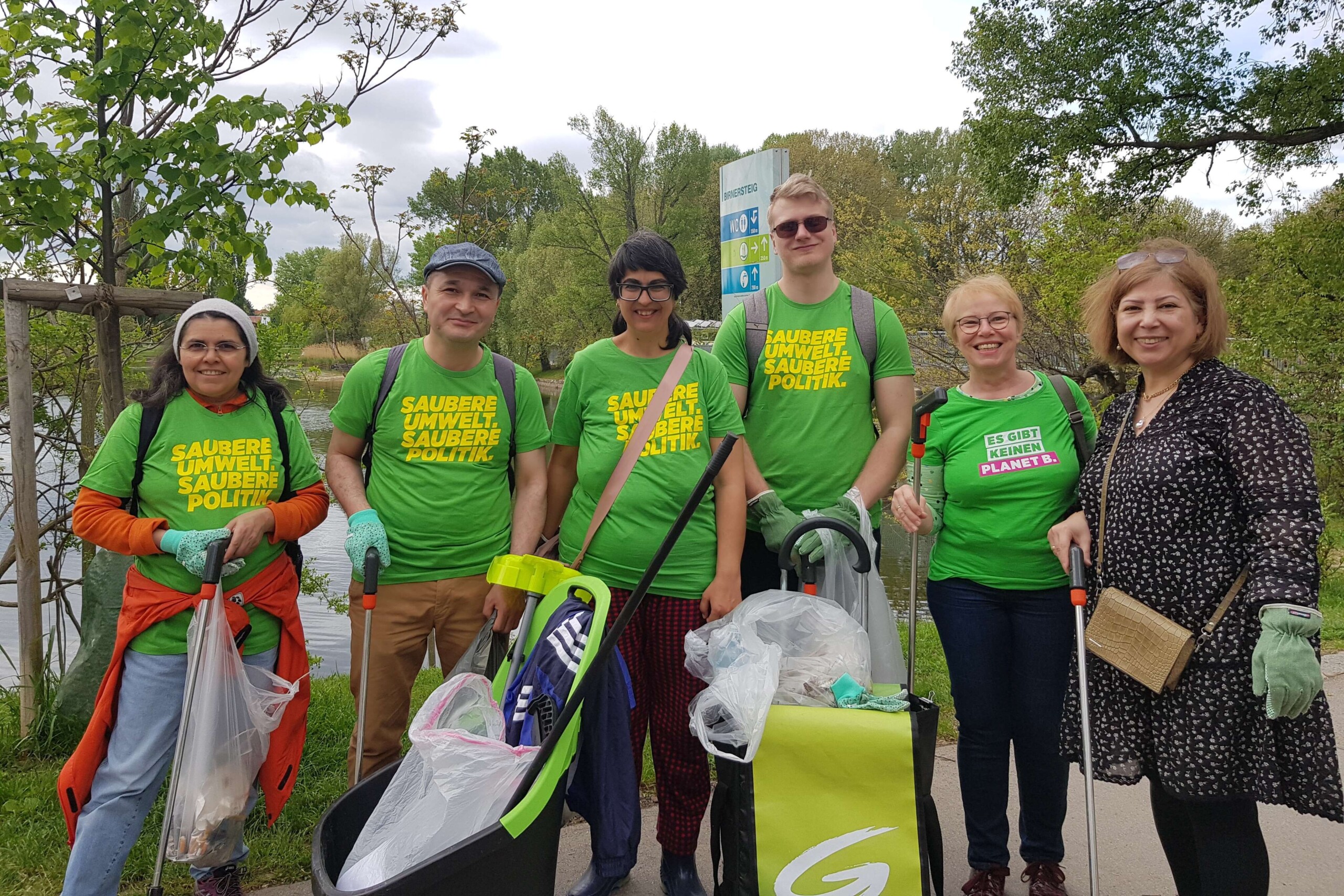 Mehrere Menschen mit Grünen T-Shirts stehen in der Natur und halten gefüllte Mistsäcke.